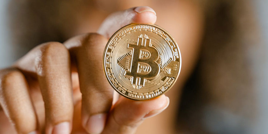 close up view of a woman in afro hairstyle holding a gold bitcoin between her fingers